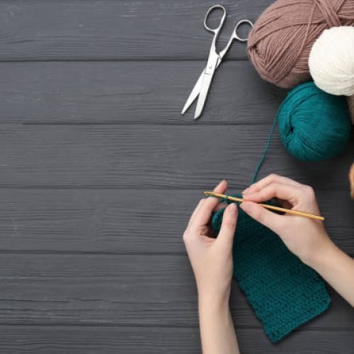 Woman crocheting with teal thread at grey wooden table, top view. Space for text